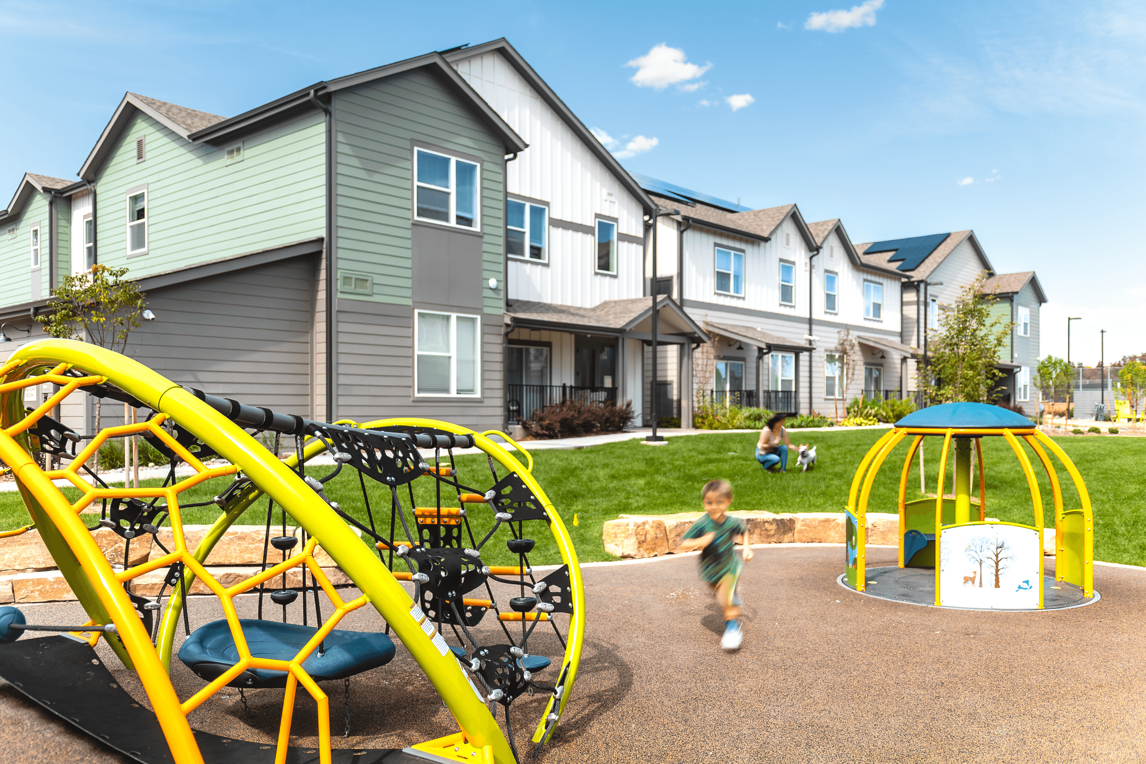 A child is playing on a playground in front of a row of houses.